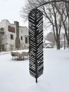 A metal sculpture in the snow in front of a building.